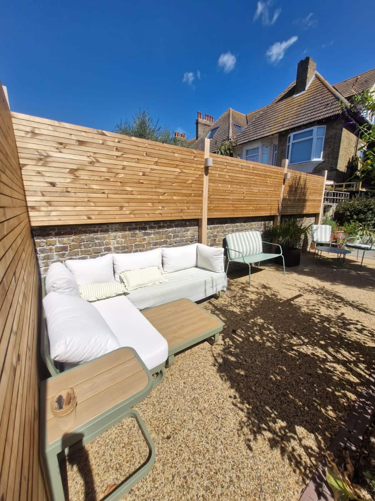 Resin-bound gravel courtyard with a slatted larch privacy screen above a brick wall and an outdoor sofa in the sun