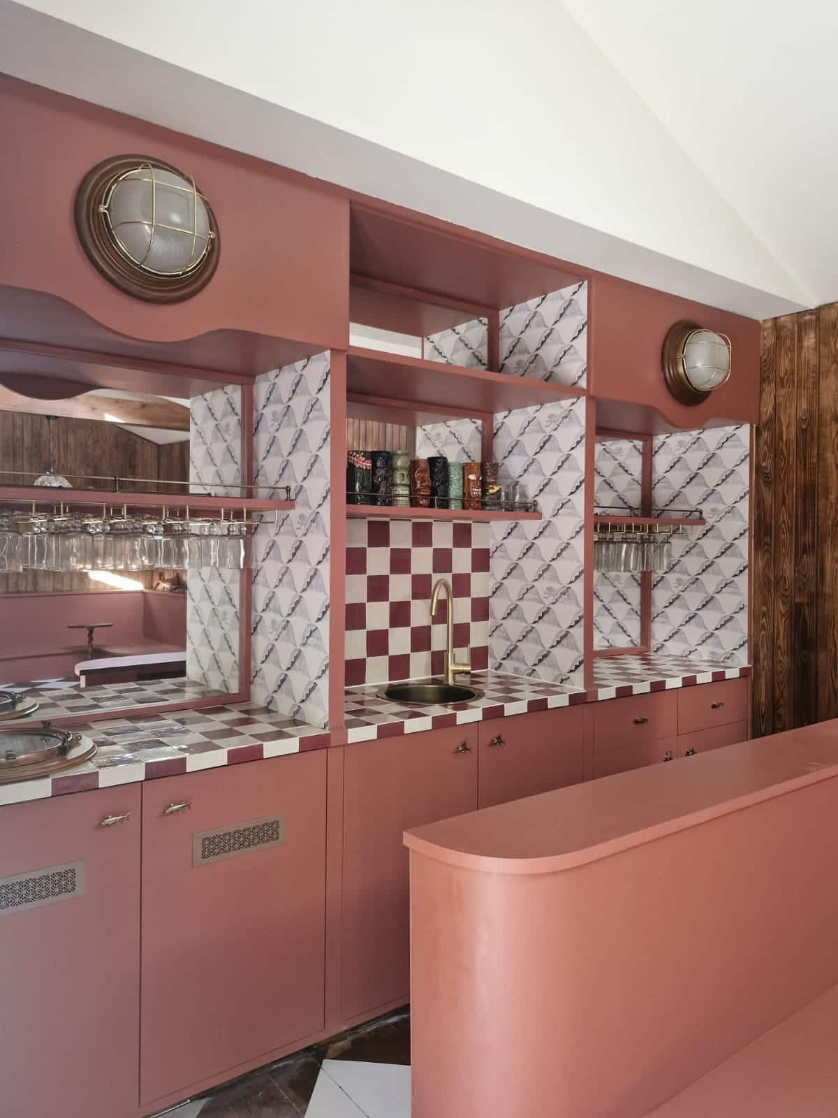 Detail of bespoke bar cabinetry in terracotta with chequered tiles, a brass tap, mirrored shelving and fish-shaped handles