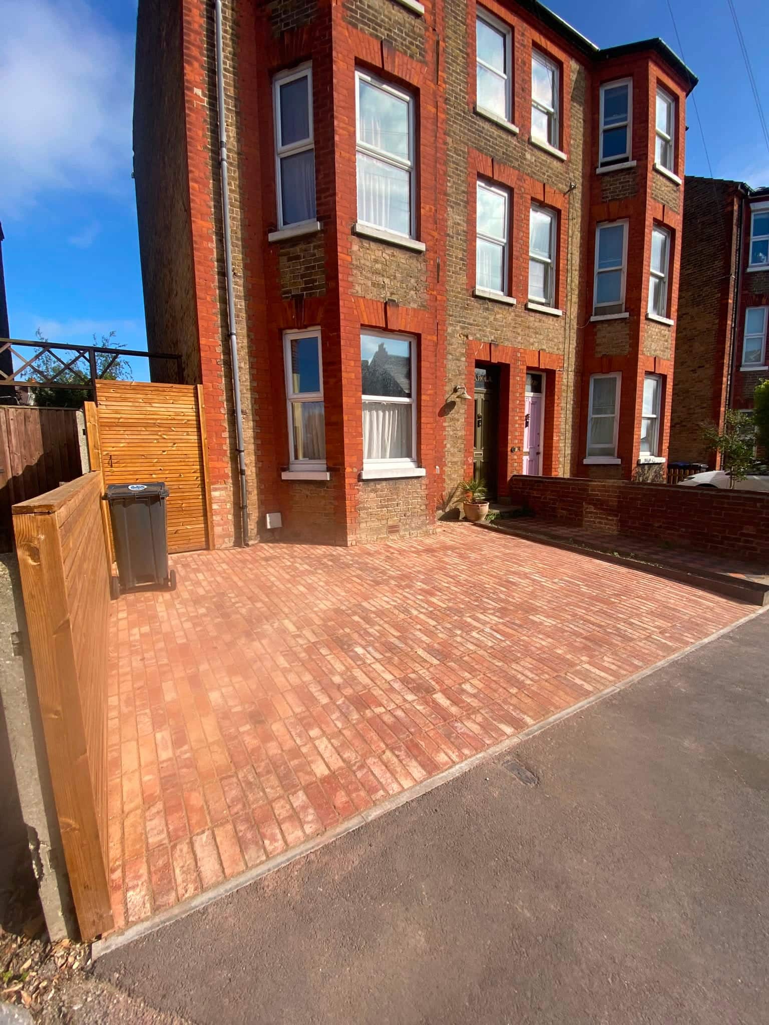 New clay-paver driveway laid in front of a three-storey red-brick period house with a slatted timber screen