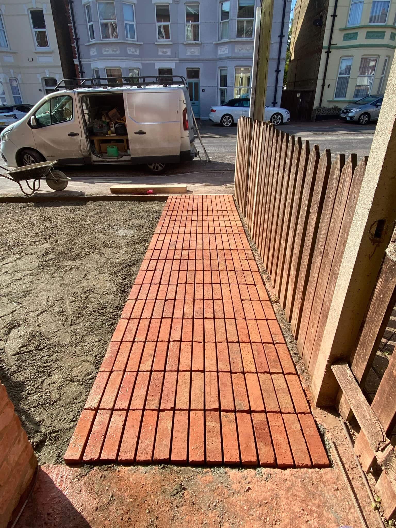 Clay pavers being laid on a compacted sand bed for a new driveway, with the Palms Build.Co van parked in the street