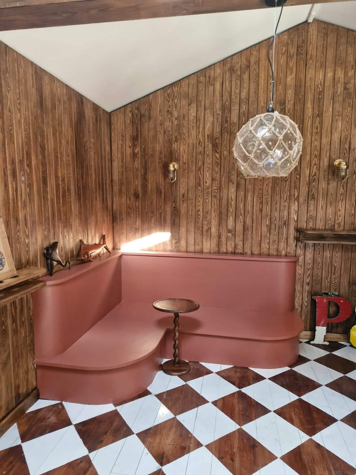 Curved built-in banquette seat painted terracotta against stained timber wall panelling, with a rope pendant light