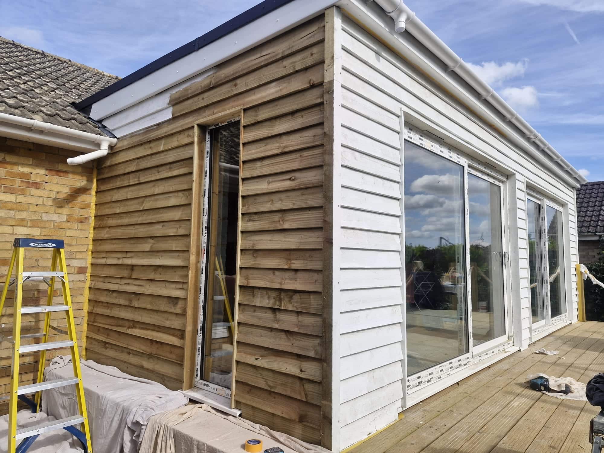 Feather-edge timber cladding being fitted and painted white on a new bungalow extension with sliding doors, during construction