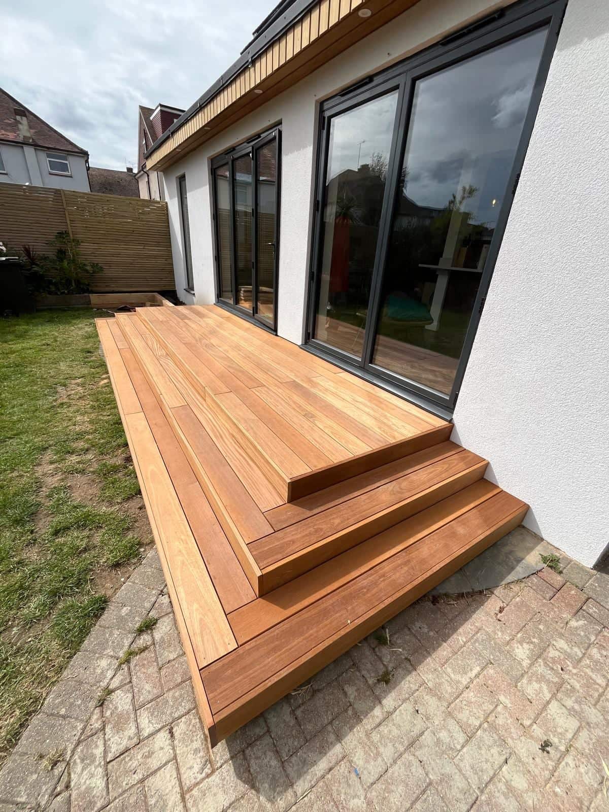 New hardwood decking and steps running along the back of a white rendered house with bi-fold doors